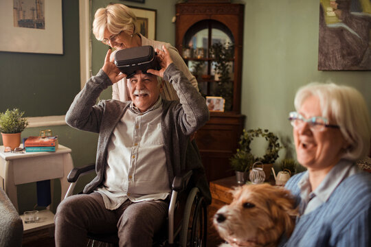 Senior man in wheelchair using vr headset at home with caregivers