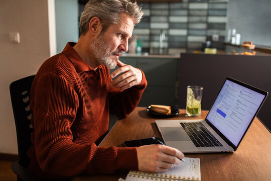 Mature man working on laptop in home kitchen