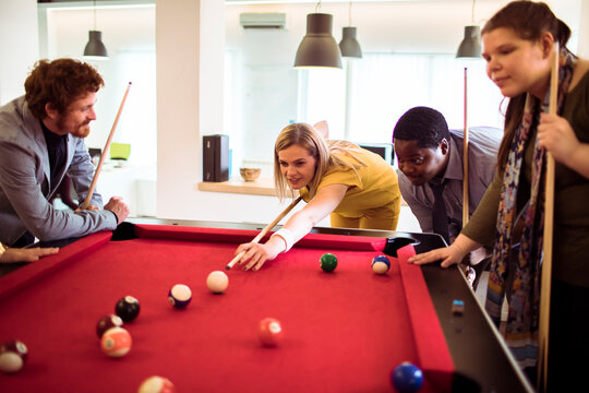 Coworkers playing pool on red table in modern office lounge
