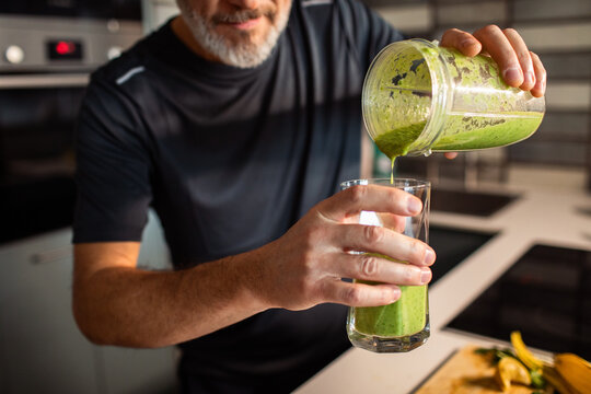 Middle-aged man pouring green smoothie in home kitchen