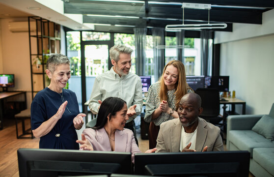 Diverse coworkers celebrating success around computers in modern office