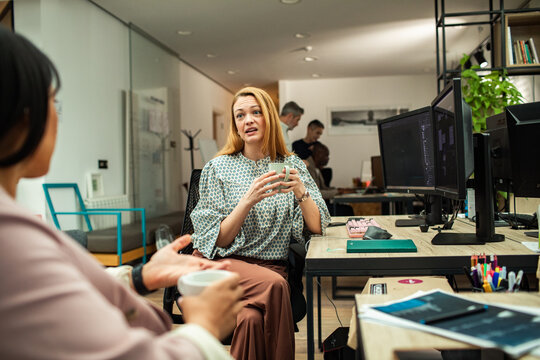 Two women discussing work over coffee in modern office