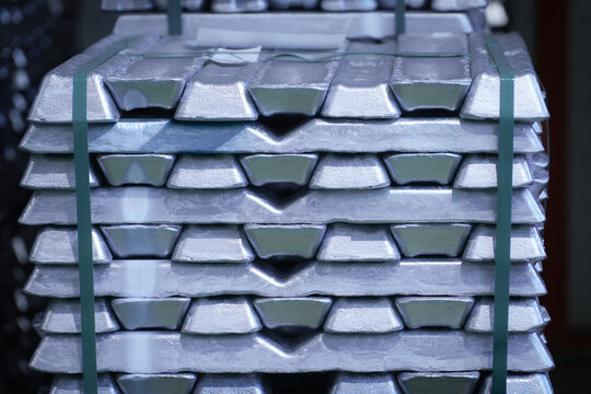 A neat stack of raw aluminum ingots bound with green plastic strapping inside an industrial foundry warehouse.