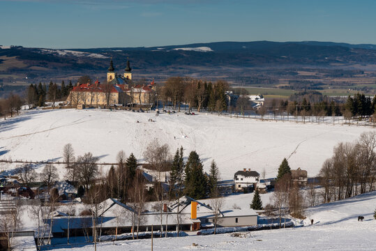A scenic winter landscape capturing the historic Monastery of the Mother of God (Klaster Hedec) on a snowy hill near Kraliky, East Bohemia, Czechia. Sunny winter day with white snow covering fields an