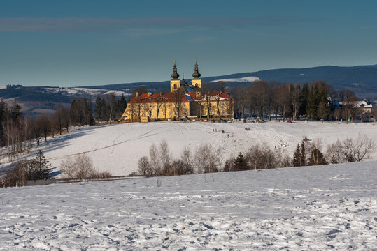 A scenic winter landscape capturing the historic Monastery of the Mother of God (Klaster Hedec) on a snowy hill near Kraliky, East Bohemia, Czechia. Sunny winter day with white snow covering fields an