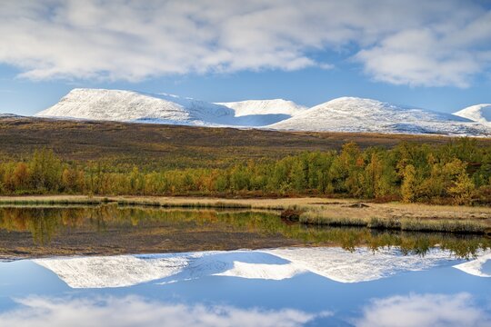 Snowy mountains of Abisko National Park reflected in small pond, autumnal fell landscape, Abisko, Lapland, Sweden