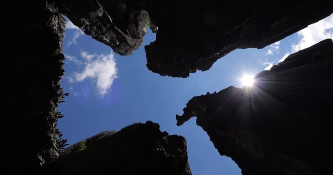 Spinning shot looking upward through jagged crevice at Shilin Stone Forest in Yunnan, China. High-contrast silhouettes of sharp towering limestone walls frame view of blue sky with sun star.