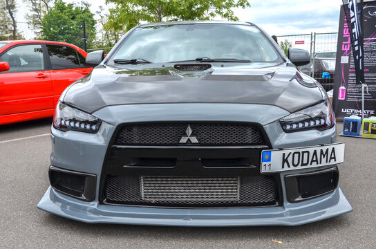 Aggressive tuner grey Mitsubishi Lancer Evolution X with a carbon fiber hood and custom LED headlights and bronze wheels, parked at car meet