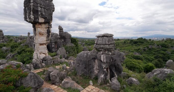 Panoramic view of green mountain landscape near Shilin Stone Forest as camera turns left to reveal unique top-heavy balancing rock shaped like thousand-year-old mushroom. Prominent geological landmark