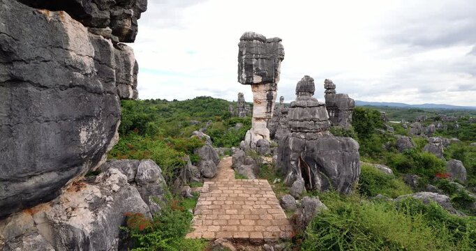 Camera turns from close view of rugged karst textures to reveal famous mushroom rock in Shilin Stone Forest. Small paved square sits at base of this towering 15-meter balancing formation
