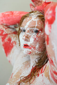Expressive portrait of a woman covered with red and white paint textures creating an intense artistic bodypainting scene with emotional gaze and abstract energy