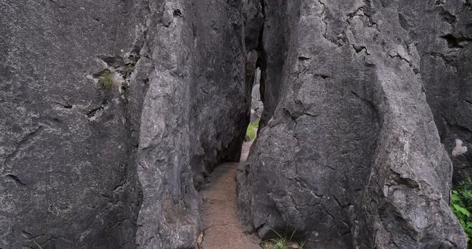 Tilt-down shot reveals narrow, uneven slit-passage through massive limestone walls in Shilin Stone Forest. Stone-paved path leads into slender karst crevice barely wide enough for person