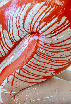 Close-up of a nude body painted with bold red and white strokes. The dynamic texture, curves, and dripping paint create an intense, sensual, and abstract visual composition full of motion