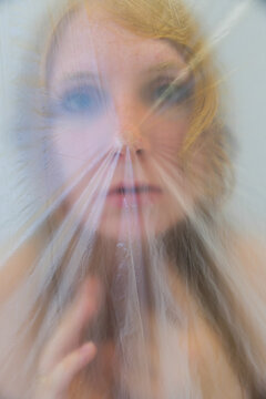 Close up portrait of a woman seen through stretched translucent plastic creating surreal blur and tension lines across her face evoking emotion fragility and dreamy abstraction.