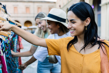 Obraz premium Multiracial young female friend smiling while shopping outdoors. Confident woman enjoying travel and leisure time in city market. Lifestyle and tourism concept.