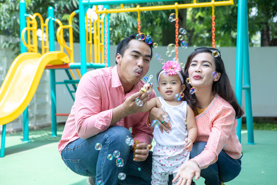 Asian Parents Blowing Soap Bubbles for Young Daughter at Colorful Playground