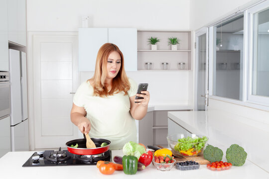 Curvy Asian Woman Checking Recipe on Smartphone While Cooking in Kitchen
