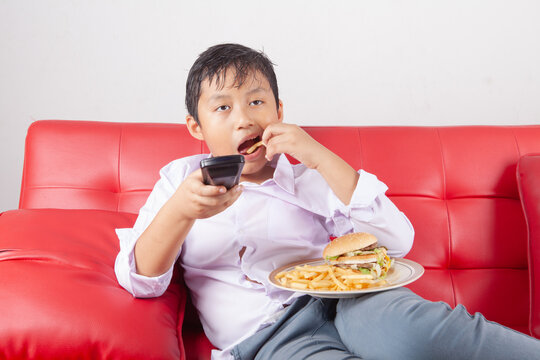 Boy on Red Couch Eating Fast Food and Watching TV with Remote Control