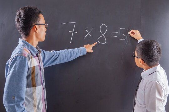 Teacher Pointing at Chalkboard While Student Solves Math Problem