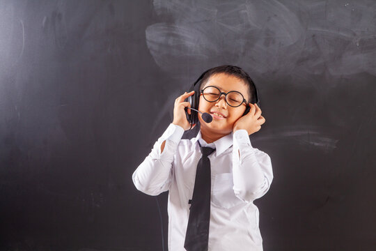 Happy Schoolboy Wearing Headset and Glasses Enjoying Music in Classroom