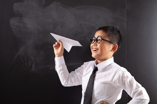 Cheerful Schoolboy with Glasses Ready to Throw Paper Airplane in Classroom