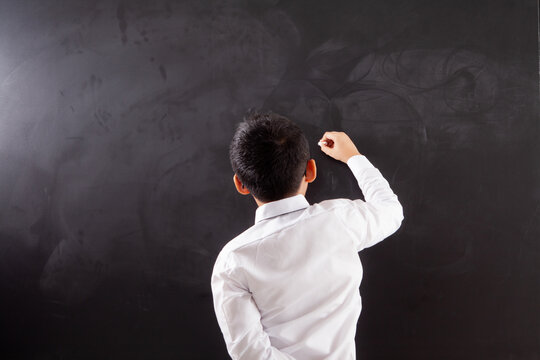 Rear View of Schoolboy Writing with Chalk on Blank Blackboard Copy Space