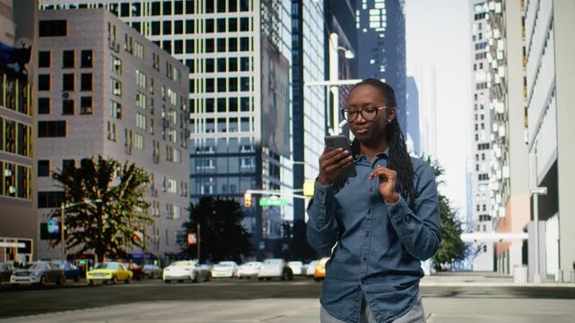 African American woman walking along city street using her smartphone, scrolling and browsing online content. Checking messages and following directions on navigation map app.