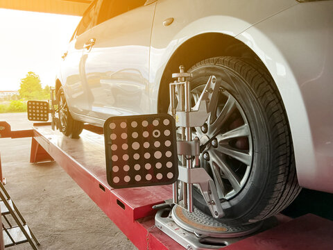 A silver car undergoes a precise wheel alignment service using advanced 3D laser target clamps on a lift in an auto repair shop.