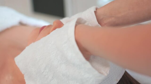 Focus on facial treatment using warm towels and gentle massage. Person enjoys the pampering at spa while relaxing on treatment table.