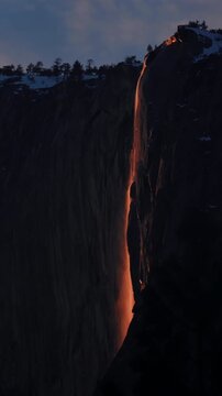 Yosemite National Park Firefall phenomenon creates stunning orange glow on Horsetail Fall cascading down El Capitan granite cliff face during February sunset with snow-covered ridge and pine trees.