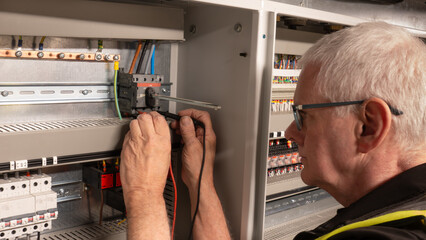 Senior electrical engineer using a multi meter to test a power isolation switch on a building management system. Mature electrical contractor inspecting a control panel control panel switch. © RCH Photographic