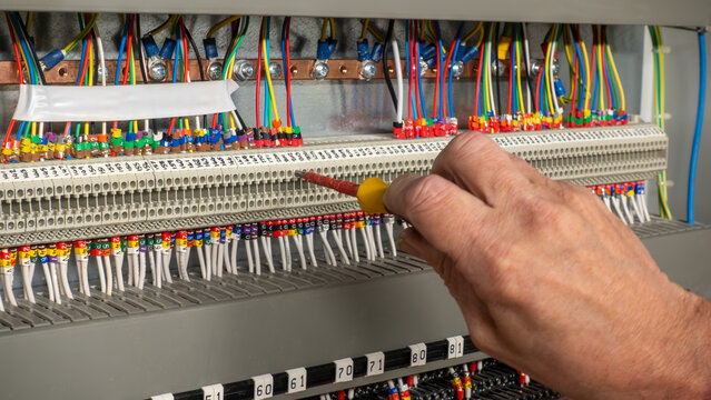 Electrical engineer using a screwdriver to check connections on connectors on a building management system. Electrical contractor inspecting a control panel a checking connections.