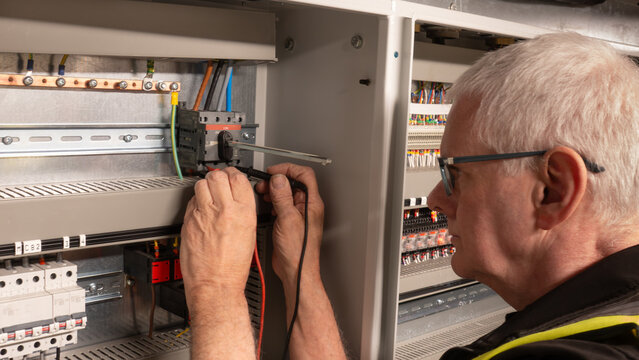 Senior electrical engineer using a multi meter to test a power isolation switch on a building management system. Mature electrical contractor inspecting a control panel control panel switch.