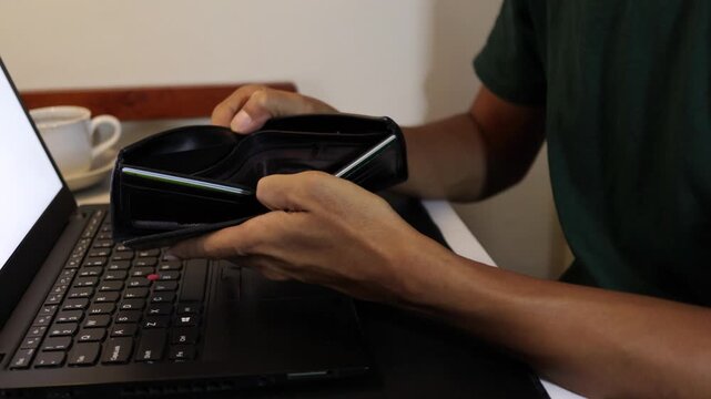 Financial crisis, no money, and bankruptcy concept with a person holding a wallet with no cash next to a computer.