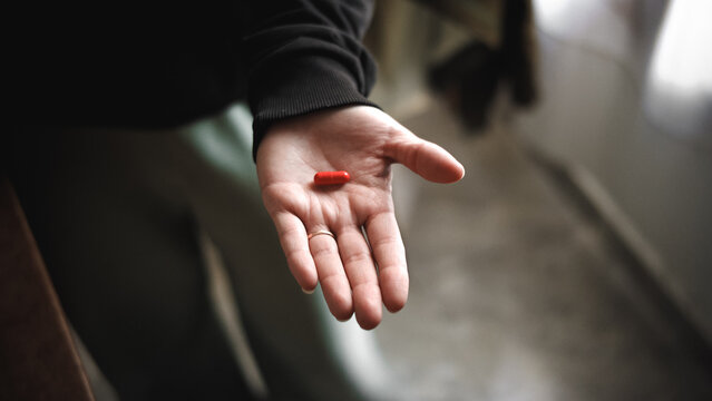 Anonymous woman&rsquo;s hand holding a red pill as part of a medical treatment. Healthcare and pharmaceutical concept.