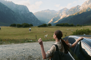Fototapeta premium Woman traveler by a car in a mountain valley, gazing toward distant peaks, backpack ready, sunlight and open air, capturing a peaceful outdoor lifestyle moment
