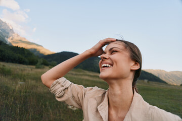 Fototapeta premium A woman enjoying the outdoors, smiling in a sunny landscape. An open field and distant mountains convey a carefree lifestyle and a strong connection with nature.