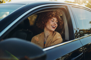 A smiling woman sits in a car window, enjoying a sunny drive with retro film color. Warm tones and...