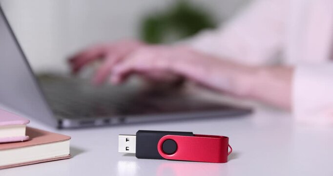 USB flash drive on desk and woman working with laptop, selective focus