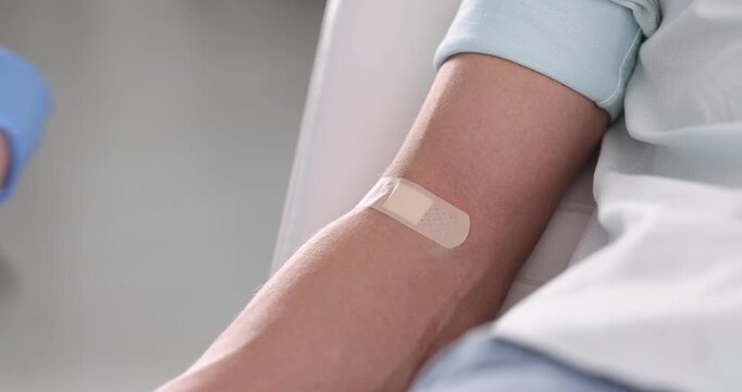 Nurse putting adhesive bandage on patient's arm and showing blood sample in clinic, closeup