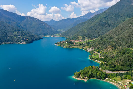 Aerial view of Lago di Ledro in northern Italy, surrounded by green mountains on a partly cloudy summer day.
