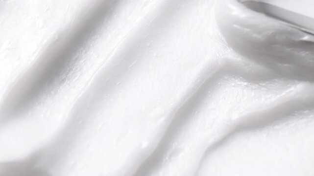 Close-up of white cosmetic cream texture being smoothed with a spatula