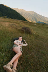 Fototapeta premium Young woman lying on grass in a mountain meadow, wearing casual clothes and boots, enjoying nature and outdoor lifestyle during daytime.