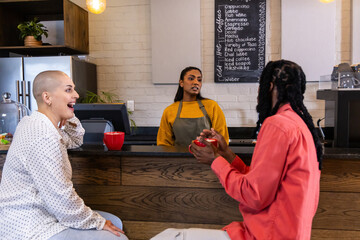 Diverse patrons talking with Indian barista in mustard sweater olive apron at counter with red mugs © wavebreak3