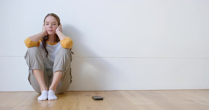 Female sitting on floor at home in yellow shirt, holding head, noticing phone, checking, copy space