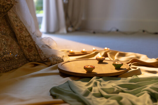 Round wooden tray is sitting on draped gold satin near curtains, holding lit clay lamps