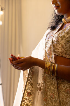Indian woman holding lit diya cradling hands in dressing room, wearing embroidered sari and bangles