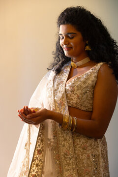 Indian woman holding small object at home wearing cream blouse or dupatta choker, bangles, bindi
