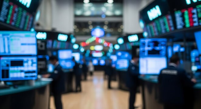 Blurred view of a busy stock exchange trading floor with multiple screens displaying financial data and people working.