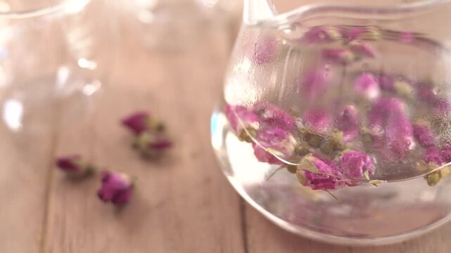 Close-up of hot organic rose tea being poured from a teapot into a clear glass cup, healthy herbal beverage for relaxation and wellness, rich in antioxidants and vitamins for healthy skin.